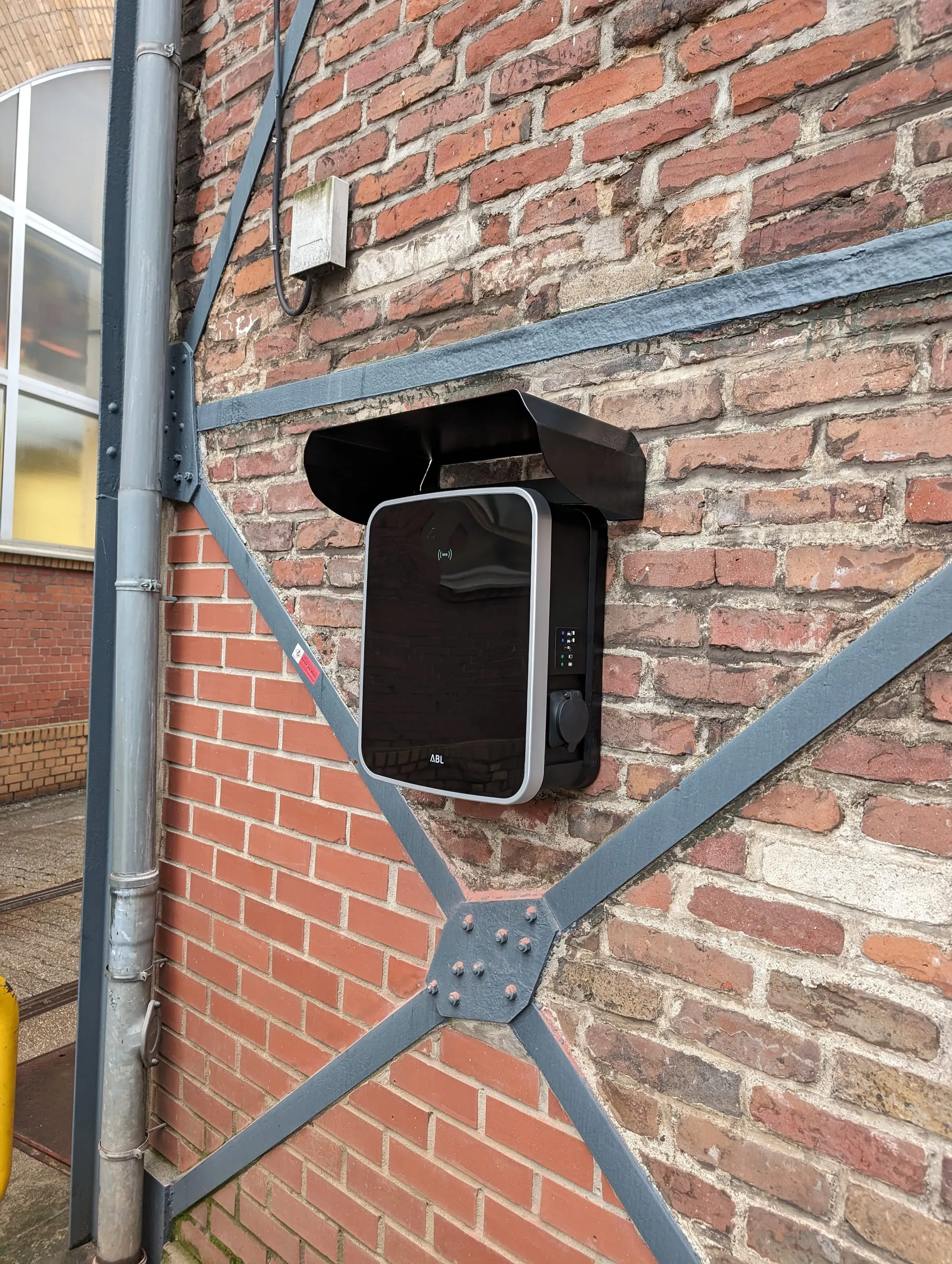 Fertig montierte Wallbox mit Wetterschutzdach an der Klinkerfassade eines Betriebsgebäudes