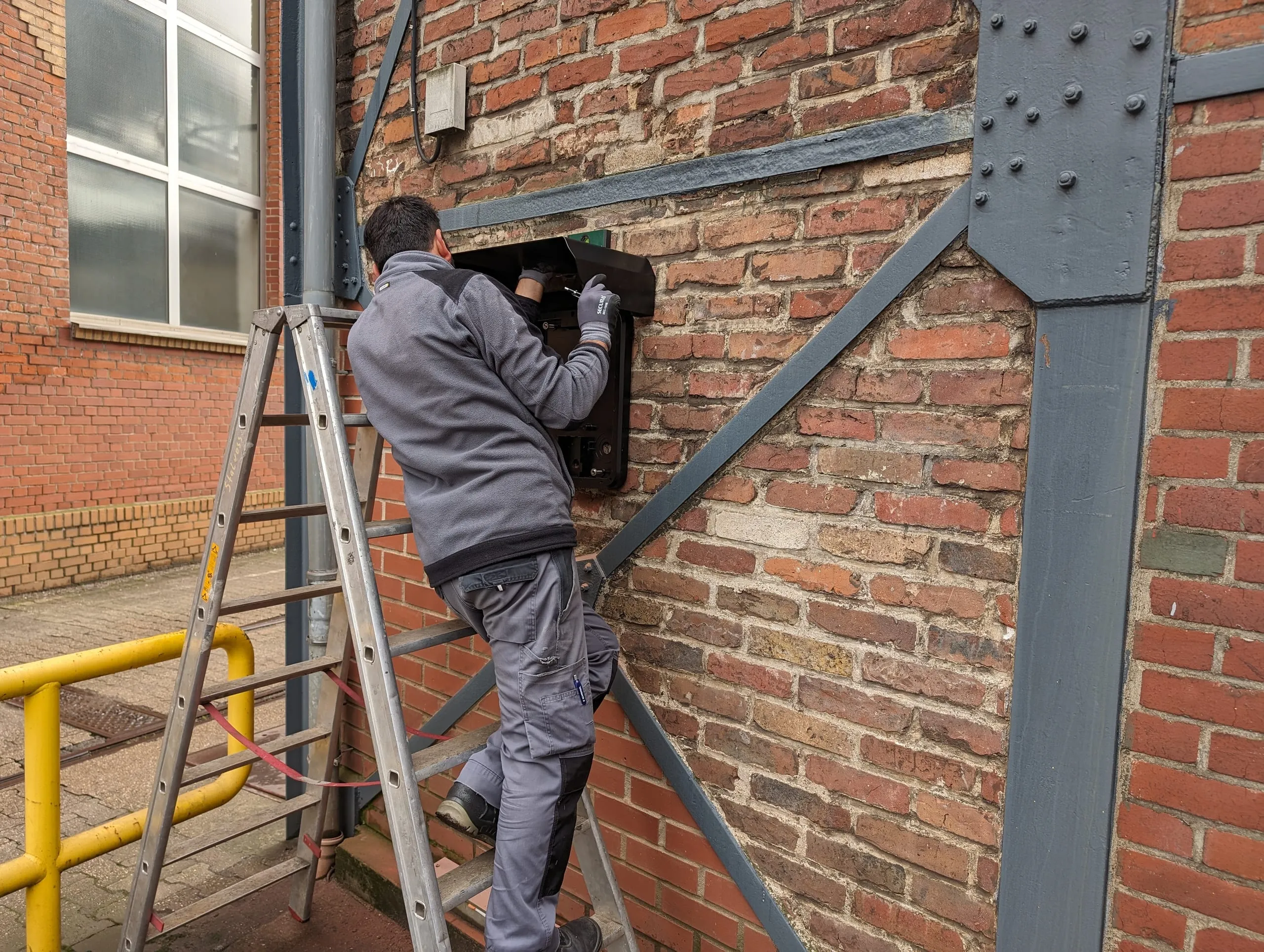 Monteur montiert eine Wallbox an der Klinkerfassade des Betriebsgeländes